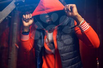 Rapper in red hoodie poses in grunge studio with cool underground decoration. Hip-hop performer, rap singer, break-dance performance
