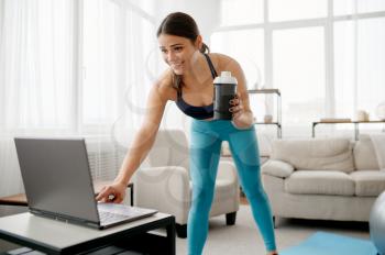 Young woman at the laptop at home, online fitness training. Female person in sportswear, internet sport workout, room interior on background