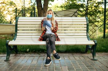 Young woman in mask sitting on bench in park, quarantine. Female person walking during the epidemic, health care and protection, pandemic lifestyle