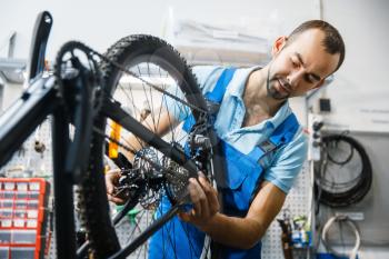 Bicycle assembly in workshop, chain installation. Mechanic in uniform fix problems with cycle, professional bike repairing service