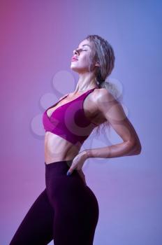 Young sexy woman with slim body poses in studio, neon background. Sportswoman at the photo shoot, sport concept, active lifestyle
