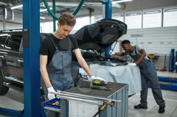Two male mechanics inspects engine, car service. Vehicle repairing garage, men in uniform, automobile station interior on background. Professional auto diagnostic