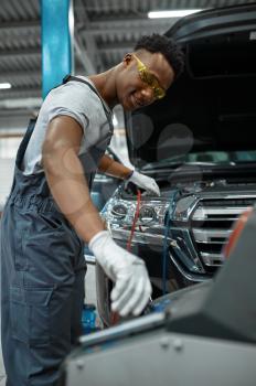 Male worker refills the air conditioner, car service. Vehicle repairing garage, man in uniform, automobile station interior on background
