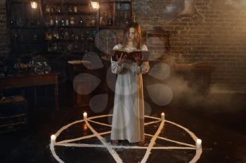 Demonic woman with book of spells standing in the magic circle, demons casting out. Exorcism, mystery paranormal ritual, dark religion, night horror, potions on shelf on background