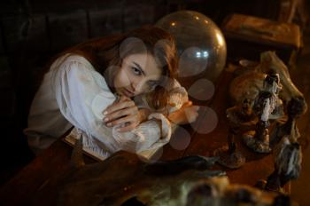 Crazy demonic woman sitting at the table, demons casting out. Exorcism, mystery paranormal ritual, dark religion, night horror, potions on shelf on background