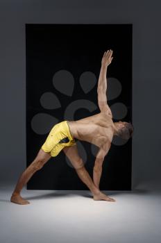 Athletic yoga doing stretching exercise in studio, grey background. Strong man practicing yogi , asana training, top concentration, healthy lifestyle