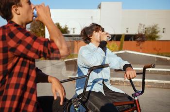 Two bmx bikers leisures in skatepark after training. Extreme bicycle sport, dangerous cycle exercise, street riding, biking in summer park