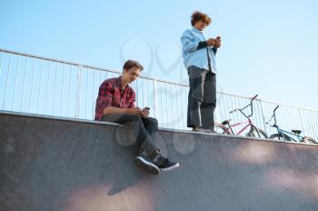 Bmx bikers, teenagers leisures on ramp in skatepark after training. Extreme bicycle sport, dangerous cycle exercise, street riding, biking in summer park