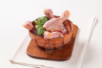 Raw chicken drumsticks in a terracotta bowl