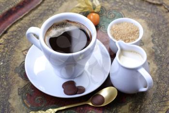 Cup of coffee, jug of cream and bowl of brown sugar