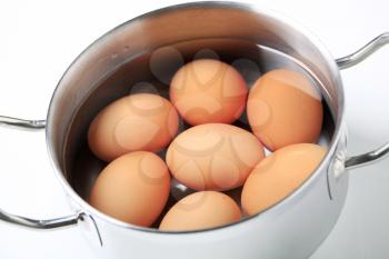 Brown eggs in water in a metal pot