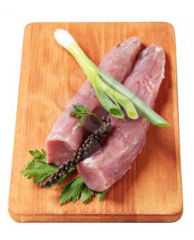 Raw tenderloin of pork, black pepper and shallot on a chopping board 