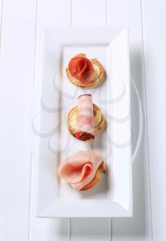 Ham and salami canapes on white plate