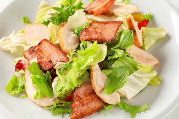 Green salad with slices of chicken breast and fried salt pork