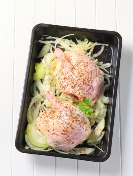 Raw duck legs with caraway and onion in a baking pan