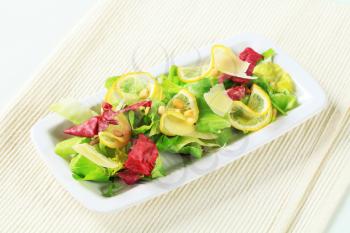 Green salad with slices of lemon, Parmesan and pine nuts