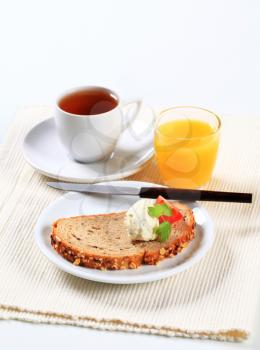 Still life of bread with cheese spread, cup of tea and orange juice