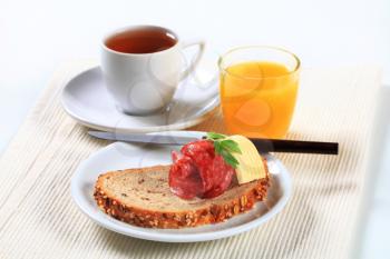Still life of bread with salami, cup of tea and orange juice