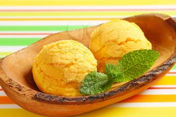 Two scoops of yellow ice-cream in olive wood bowl