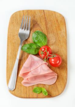 Sliced ham, tomatoes and basil leaves on cutting board