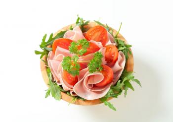 Sliced ham with rocket salad and tomatoes in a wooden bowl