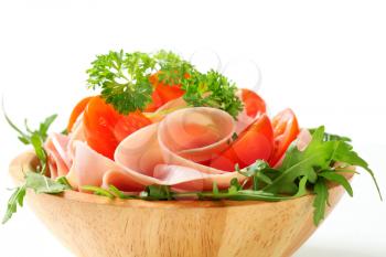 Sliced ham with rocket salad and tomatoes in a wooden bowl