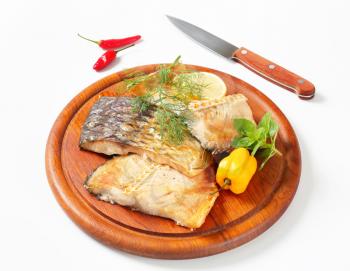 Oven-baked carp fillets on round cutting board