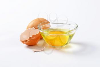 Fresh egg white and yolk in glass bowl, whole egg and eggshell
