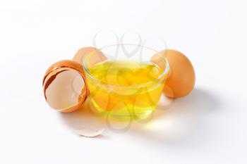 Fresh egg whites and yolks in glass bowl, one whole egg and empty eggshells