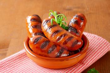 bowl of grilled sausages with parsley and rosemary on checkered tablecloth