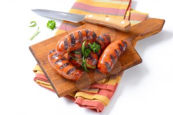 grilled sausages with parsley and rosemary on wooden cutting board
