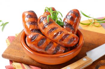 bowl of grilled sausages with parsley and rosemary on wooden cutting board
