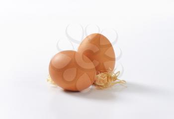 two organic eggs with straw on white background