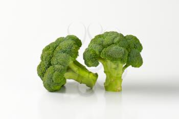 two fresh broccoli heads on off-white background