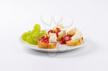 slices of fresh bread with brie cheese, walnuts, jam and grapes on white plate