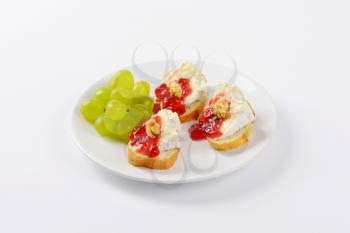 slices of fresh bread with brie cheese, walnuts, jam and grapes on white plate
