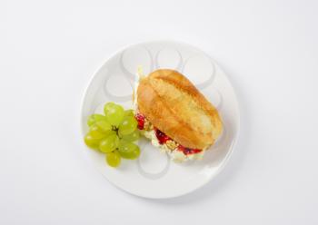 small baguette with brie cheese, walnuts, jam and grapes on white plate