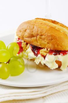 small baguette with brie cheese, walnuts, jam and grapes on white plate