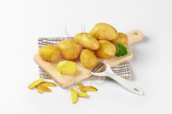 fresh potatoes and peeler on wooden cutting board