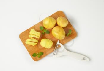 raw potatoes and peeler on cutting board