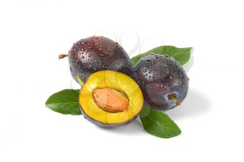 two whole plums and half a plum with stone on white background