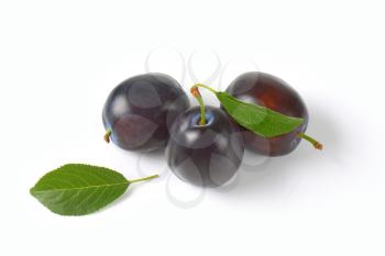 three ripe plums with leaves on white background
