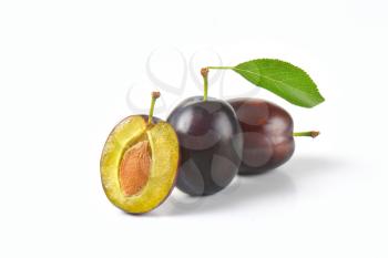two whole plums and half a plum with stone on white background