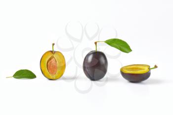 whole and halved plums on white background