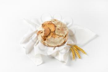 round loaf of bread on white napkin and ripe grain ears