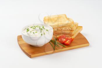 pile of toasted white bread slices and bowl of  creamy spread with chives