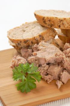 pieces of canned tuna and sliced seeded bread roll on cutting board
