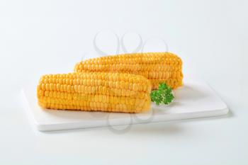 two boiled corn cobs on white cutting board