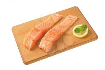 two raw salmon fillets on wooden cutting board