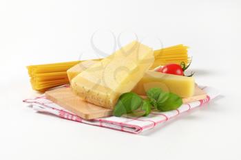 wedges of parmesan cheese on wooden cutting board and bundle of raw spaghetti